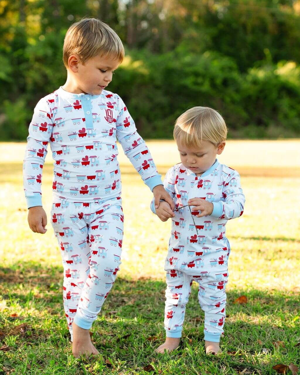 Two children wearing matching pajamas with a pattern of cars and stars, standing outdoors on grass.