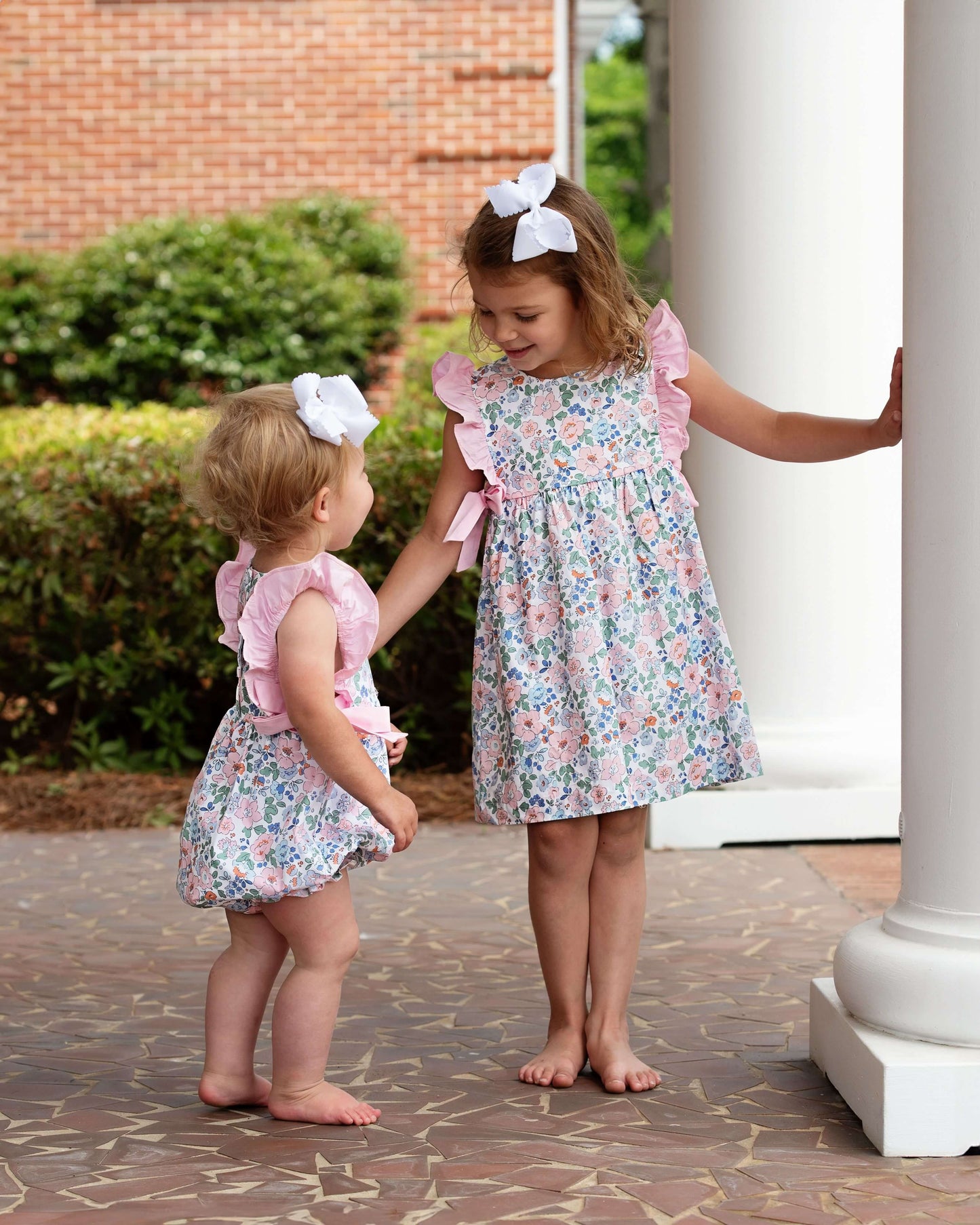 Two young girls in floral dresses standing on a patio.