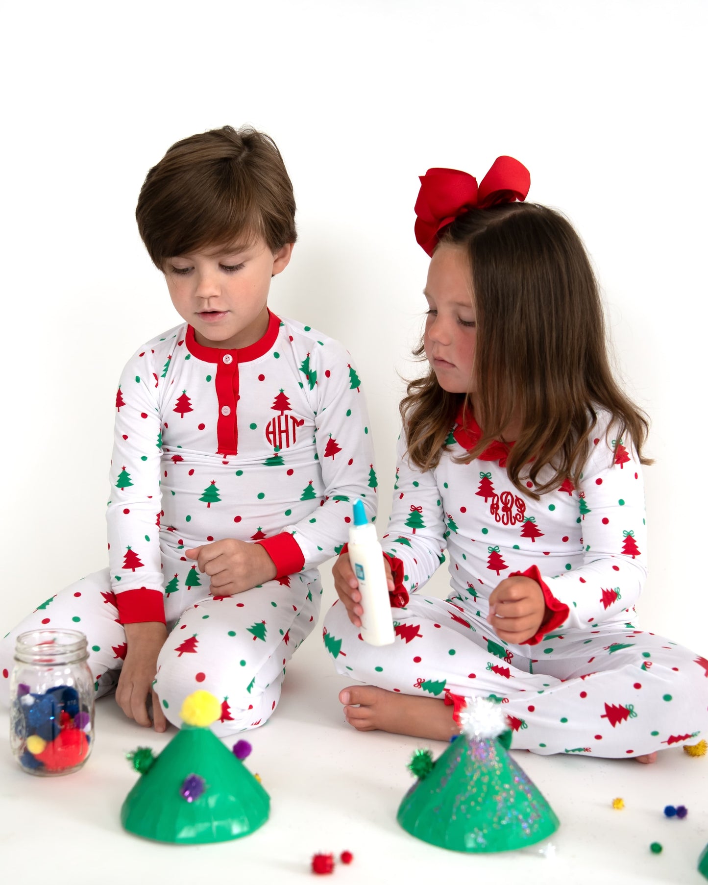 A boy and a girl in matching Christmas pajamas making crafts.