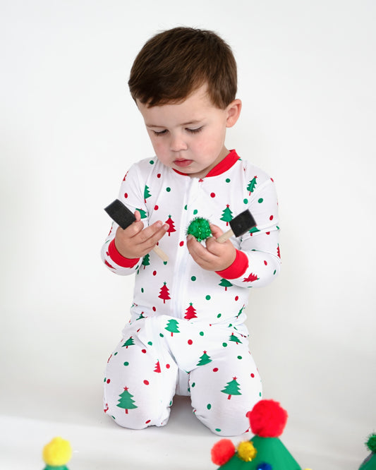 A young boy in holiday pajamas holding paint brushes.