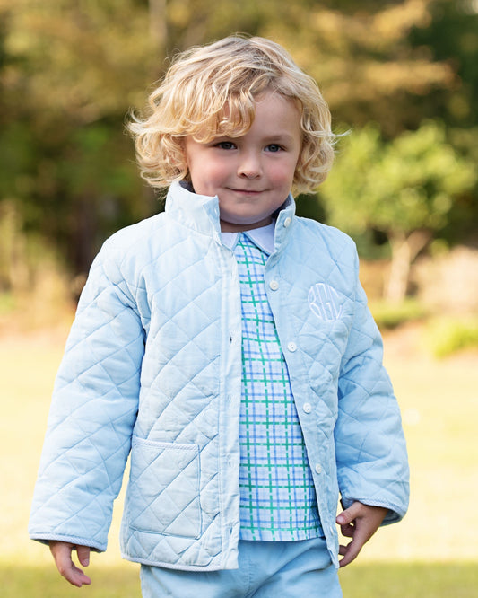 A young boy standing outside wearing a blue quilted coat with a white monogram