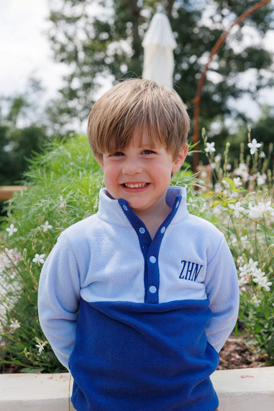 A young boy standing outside wearing a navy and blue fleece jacket with snaps and a navy monogram