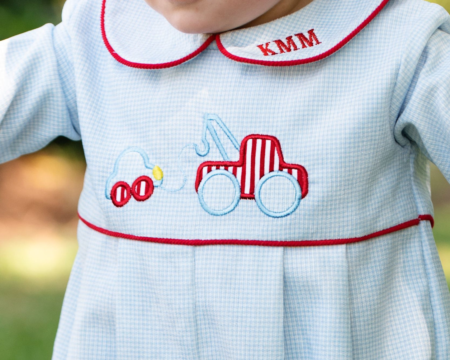 Baby dress with embroidered designs and 'KMM' monogram on a blurred green background