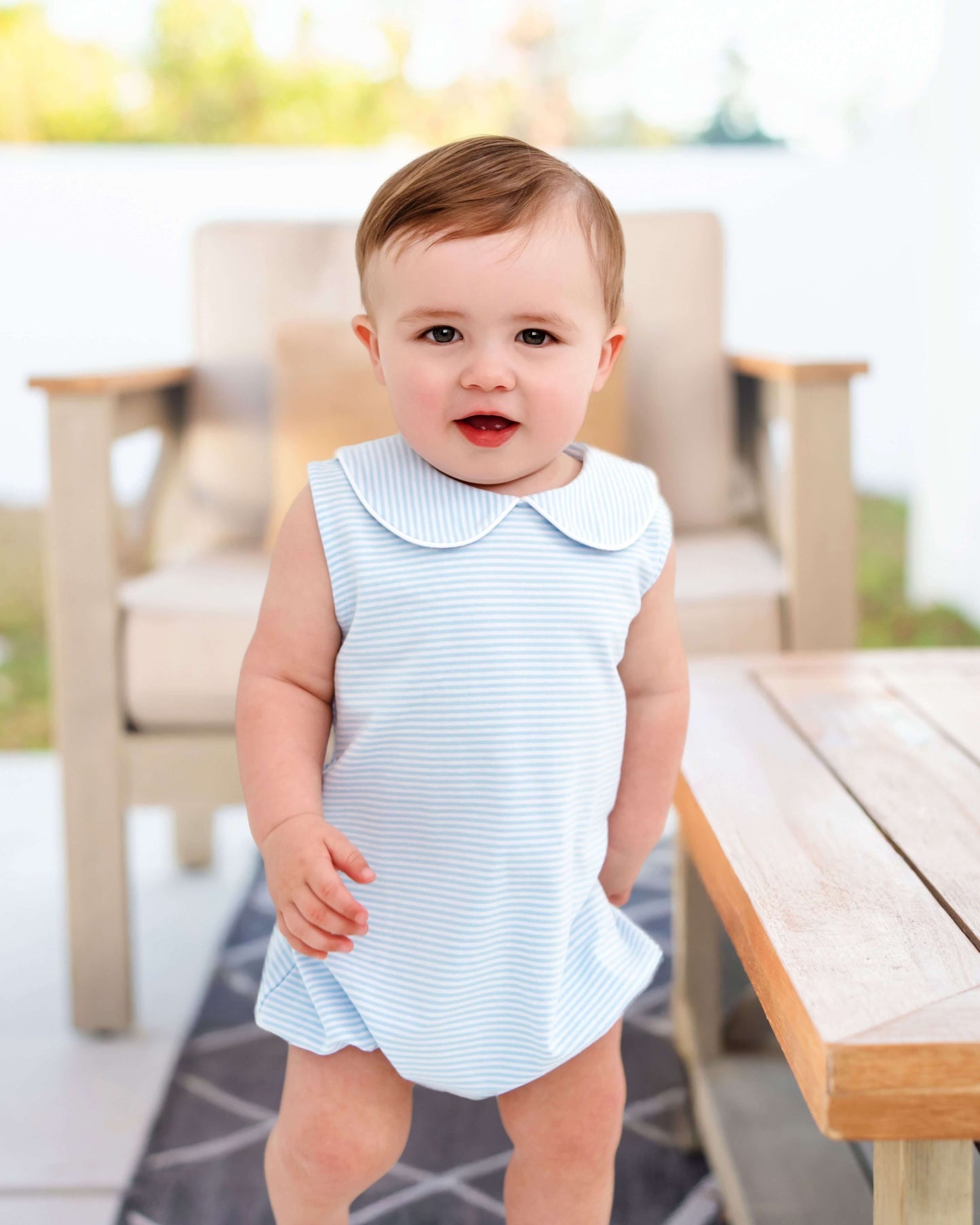 Baby in a light blue dress standing outdoors with blurred background