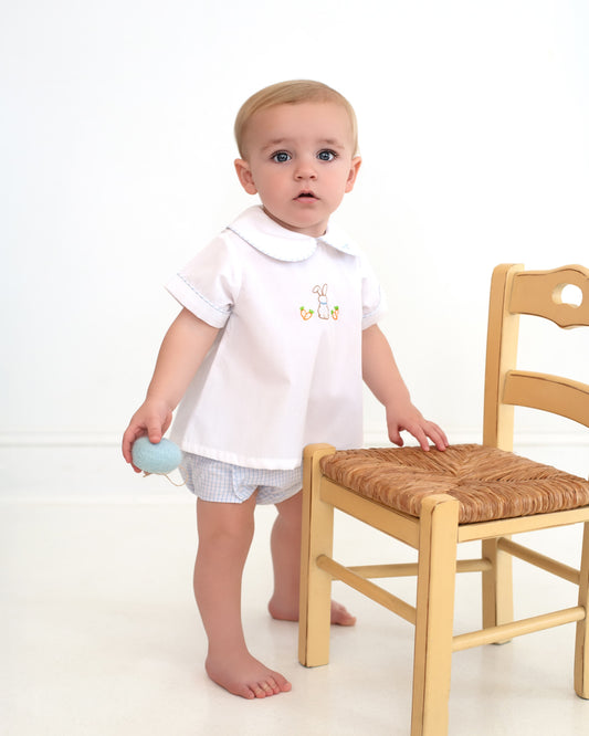 Baby in a white shirt standing next to a wooden chair on a white background
