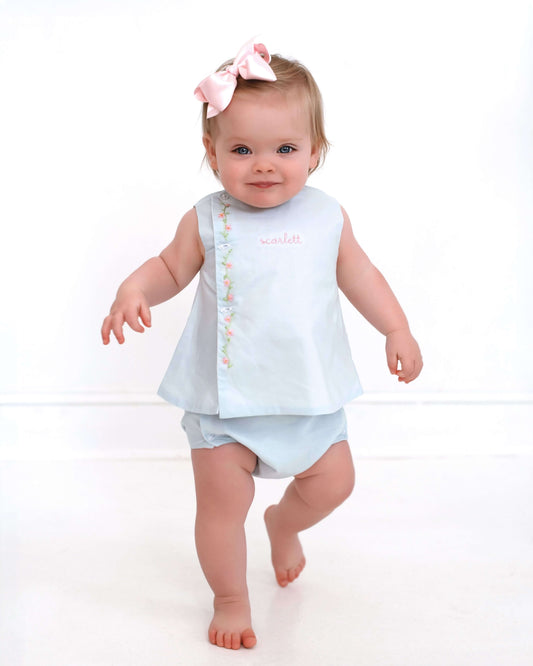 Baby in light blue outfit with pink bow on a white background