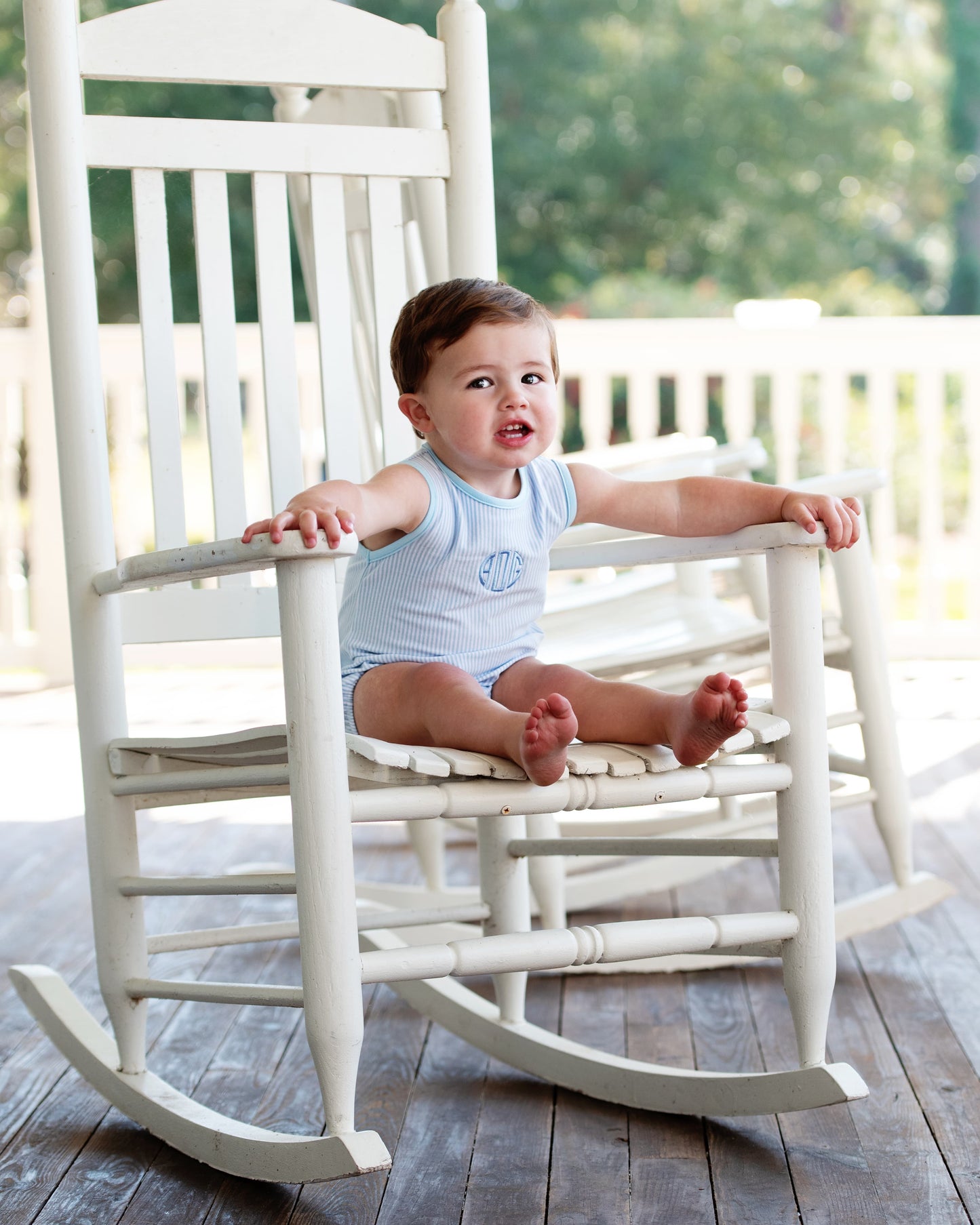 Baby sitting on a white rocking chair wearing a blue bubble, outdoors