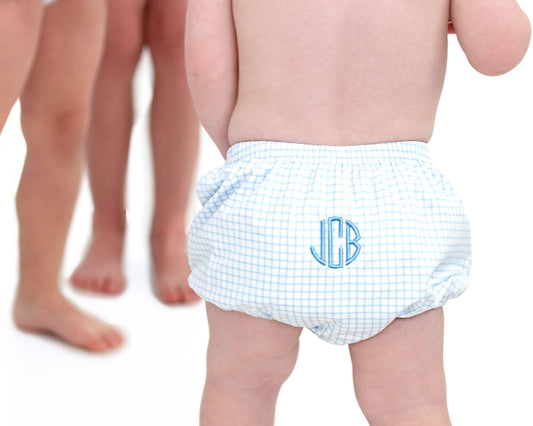 Baby wearing a light blue checkered diaper with 'JCB' monogram on a white background
