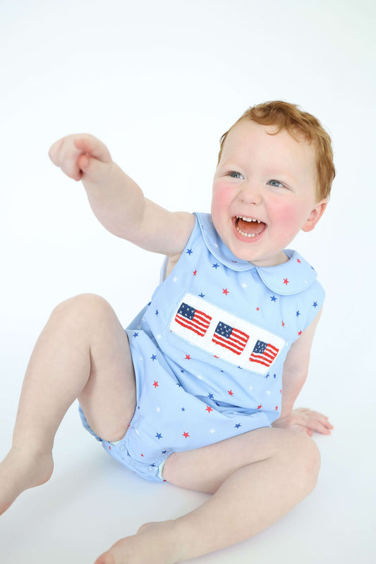 Baby wearing a light blue outfit with American flag designs on a white background