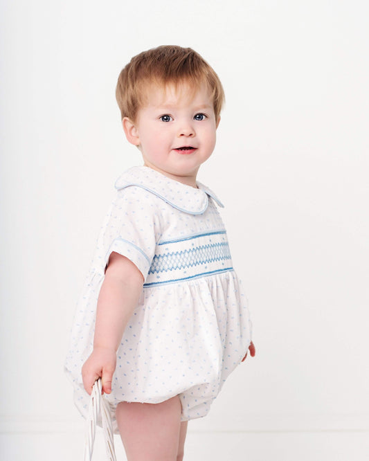 Baby wearing a white dress with blue patterns on a white background