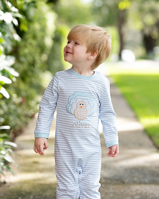 Boy standing on a sidewalk wearing a blue outfit with a turkey in the center