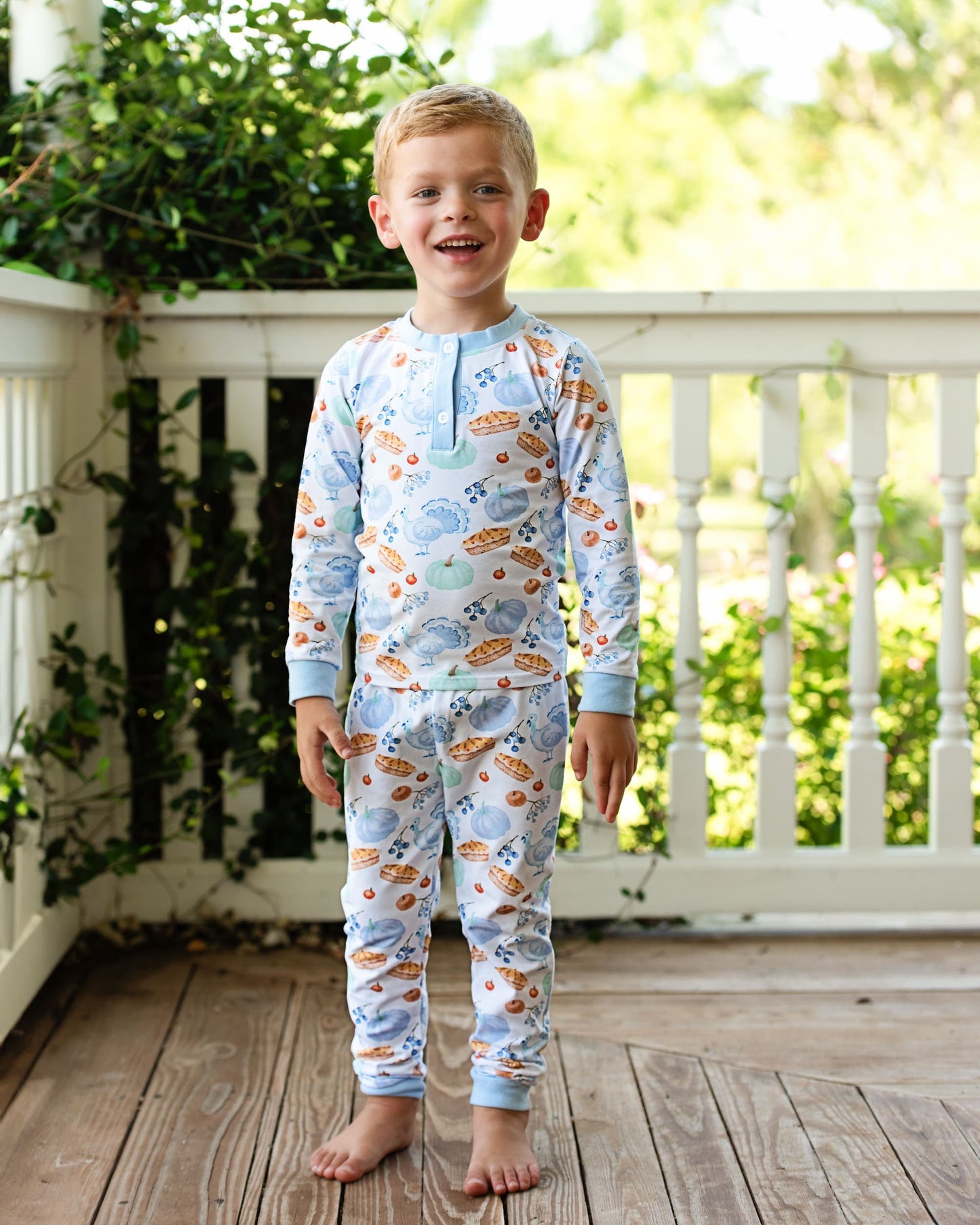 Boy wearing a blue pajama set with Turkey print on a wooden deck.