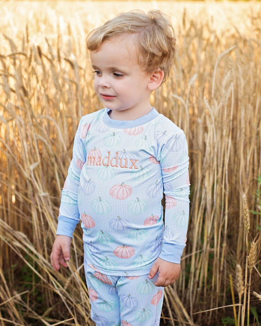 Boy wearing a light blue long-sleeve pajama set with 'maddux' printed on it, standing in a field of tall grass.