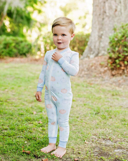 Boy wearing a light blue zipper pajama with pumpkin pattern outdoors on grass