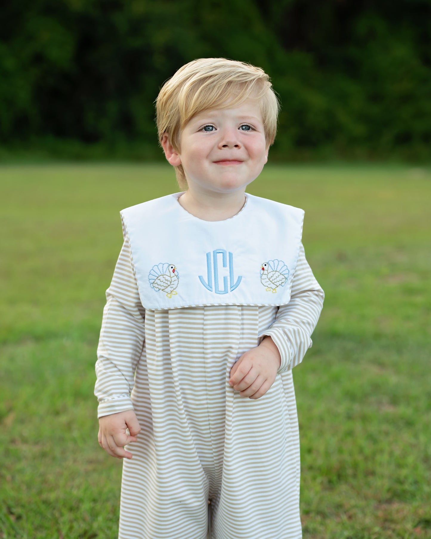 Boy wearing a striped khaki long romper with turkey and monogram "jCl"