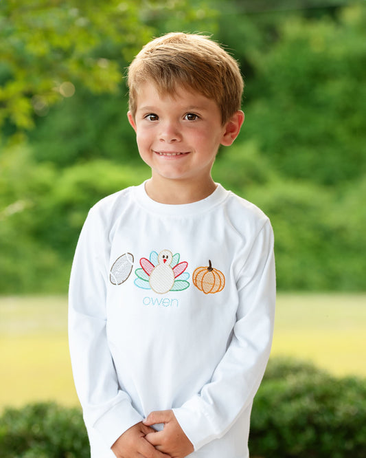 Boy wearing a white tshirt with a turkey, football and pumpkin embroidered on it