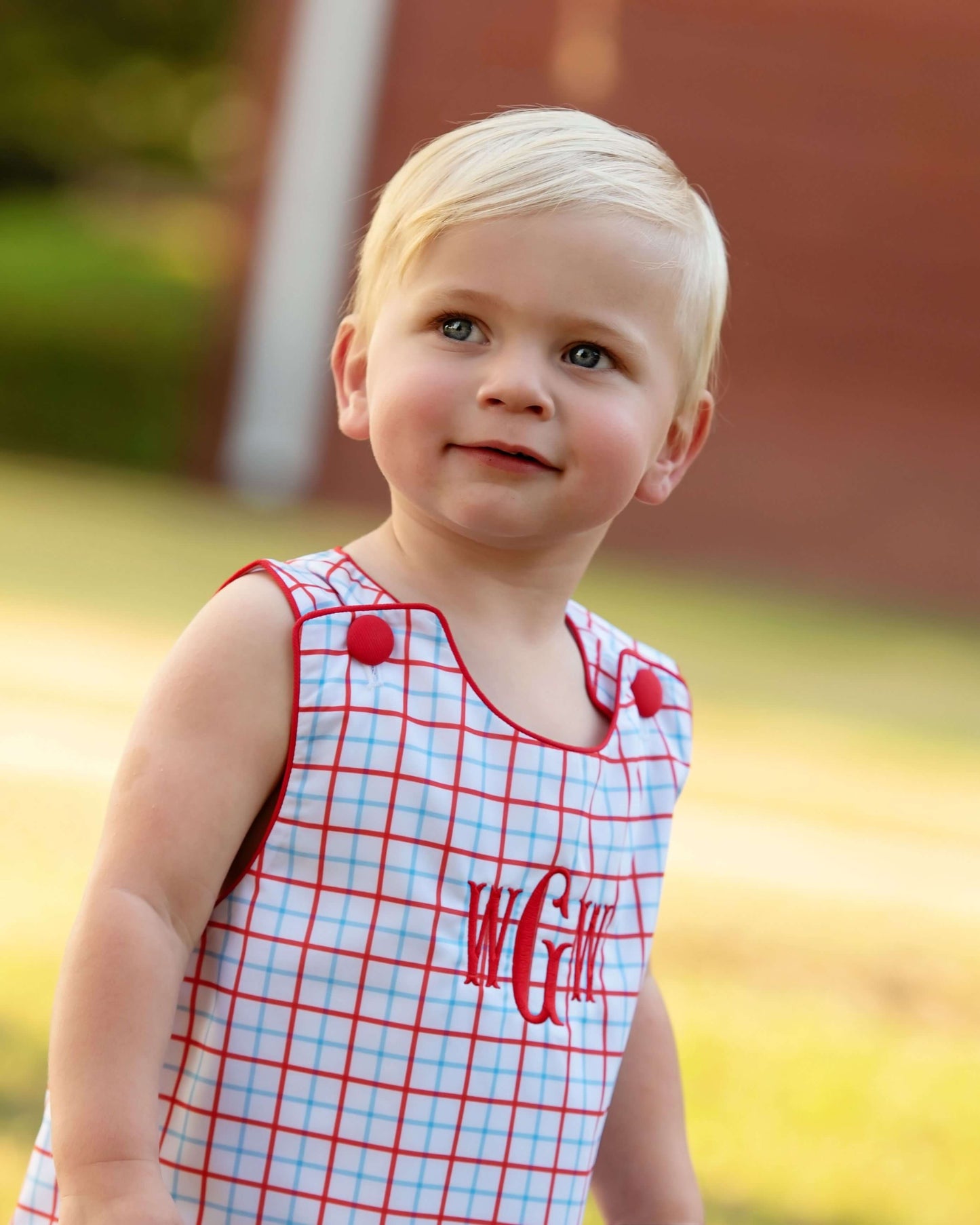 Boy wearing a windowpane outfit with red buttons and a monogram on the chest.