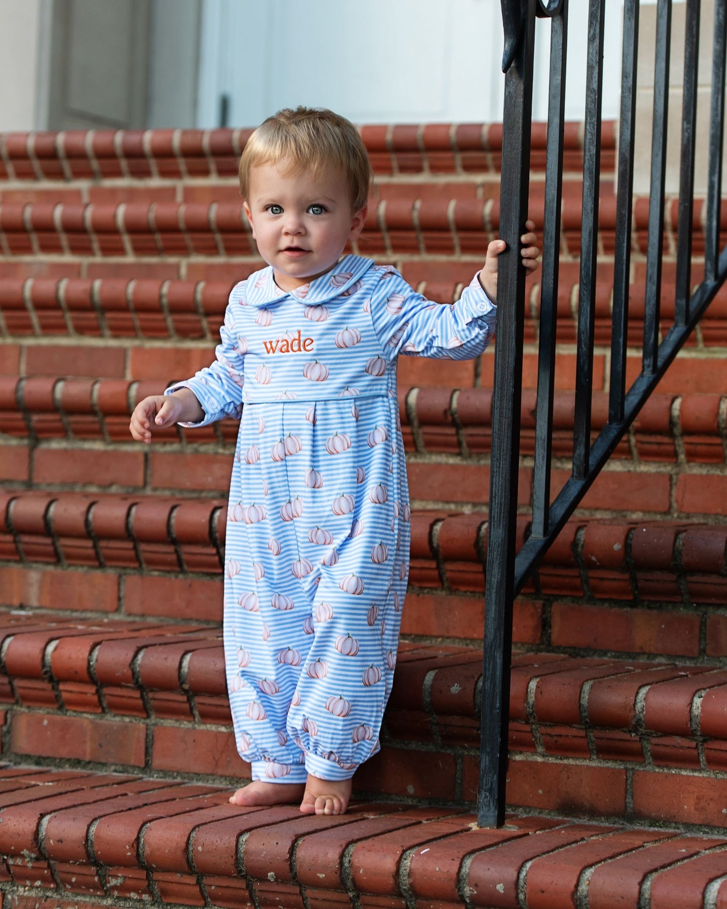 Child in a blue onesie with pumpkin patterns on red brick steps