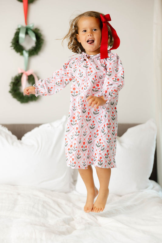 Child in a floral nightgown standing on a bed with Christmas decorations in the background