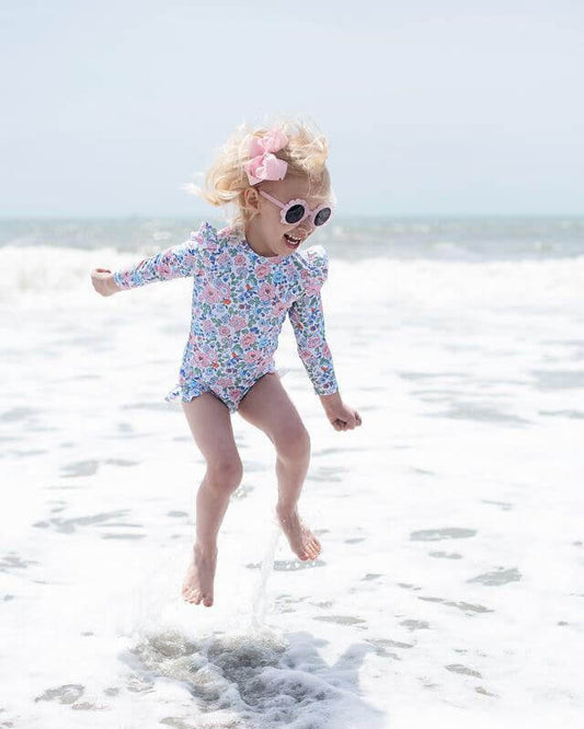 Child in a floral swimsuit playing in the ocean.
