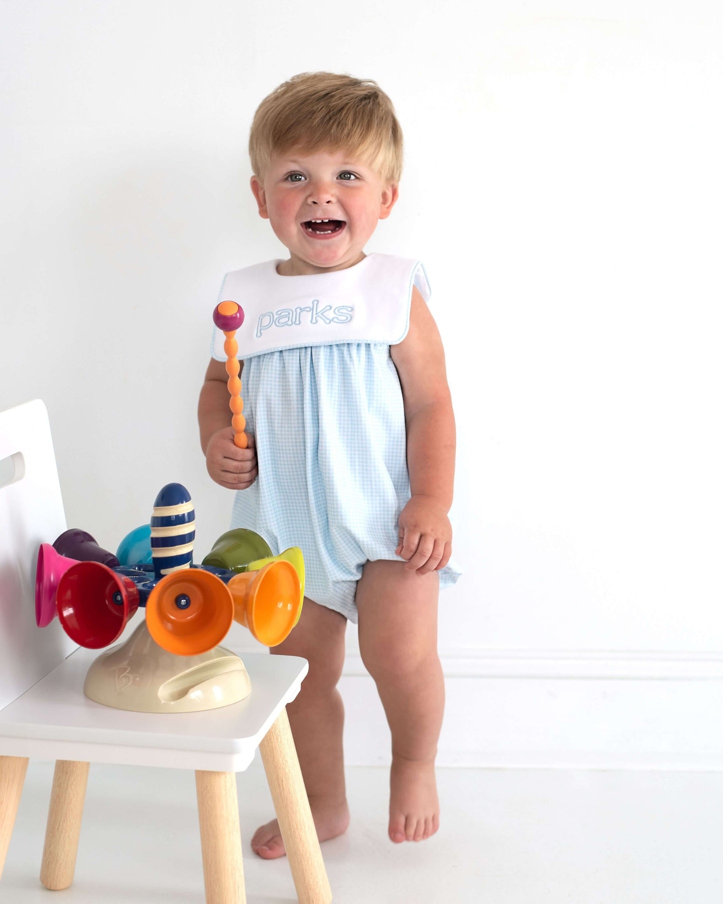 Child in a light blue romper with colorful toys on a white background