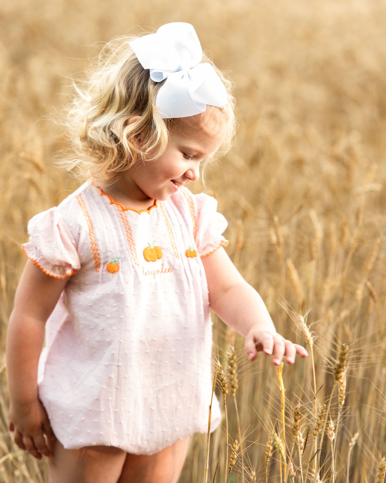 Child in a pink bubble with orange trim standing in a field of tall grass.