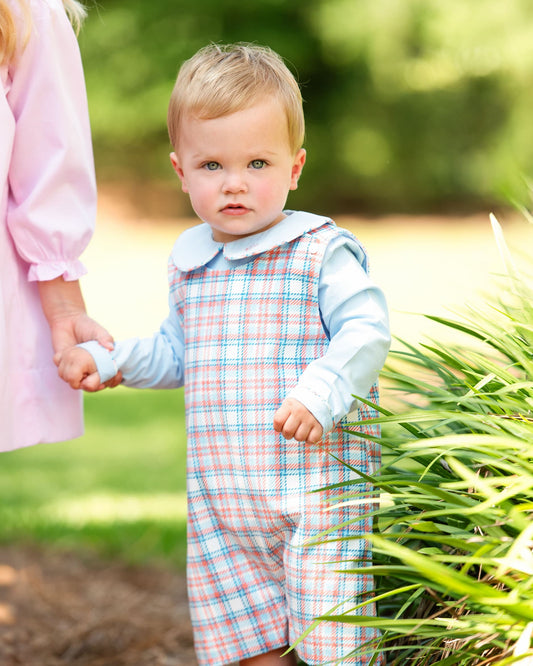 Child in a plaid outfit standing outdoors with a blurred background