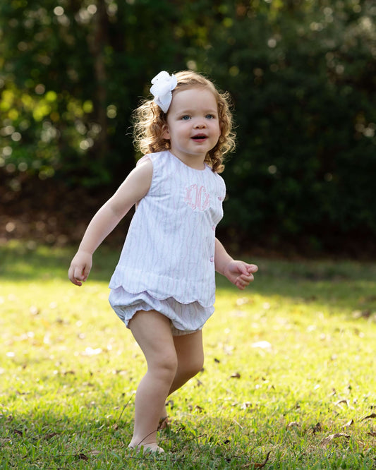Child in a white floral diaper set with a bow standing on grass