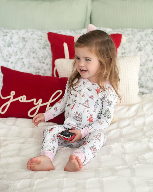 Child in pajamas sitting on a bed with Christmas-themed pillows