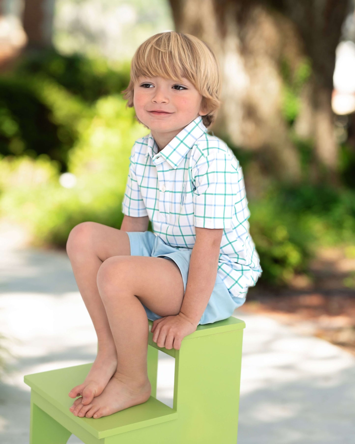 Child sitting on a green step outdoors with blurred greenery in the background