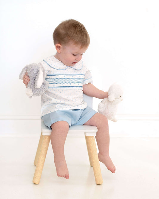 Child sitting on a small stool holding stuffed animals against a white background