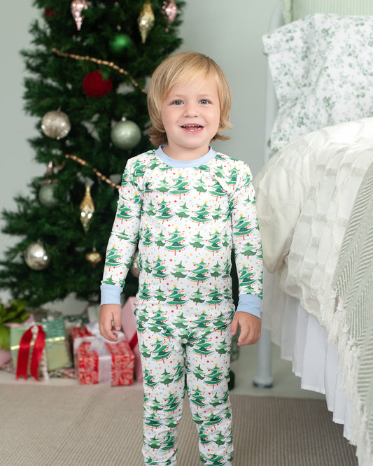 Child wearing Christmas-themed pajamas in a room with a decorated tree and presents.