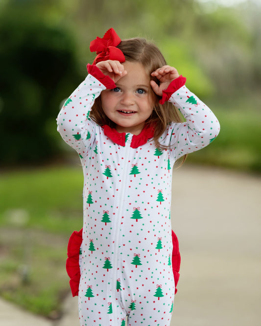 Child wearing a Christmas-themed onesie with red bows outdoors.