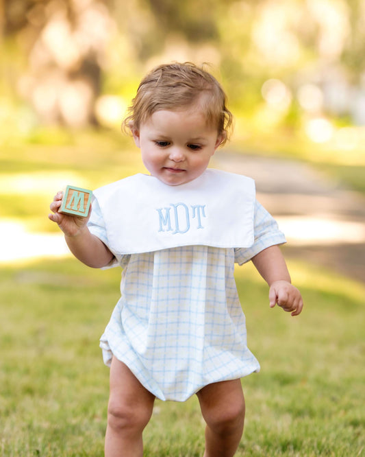 Child wearing a bib with 'MDT' outdoors on a sunny day
