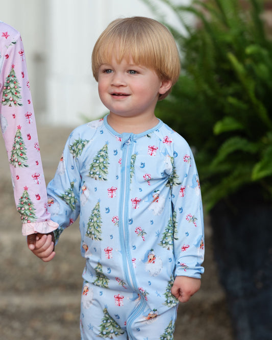 Child wearing a blue Christmas-themed pajama with pink sleeves featuring tree designs.