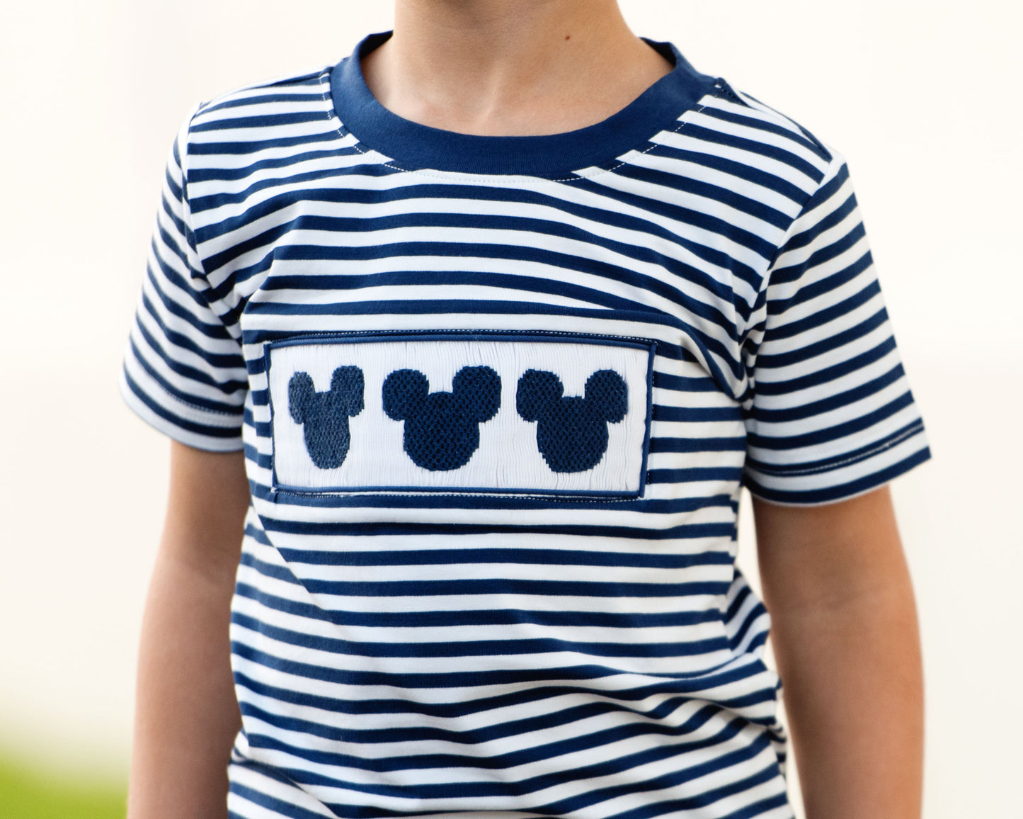 Child wearing a blue and white striped shirt with a Mickey Mouse patch on a blurred background