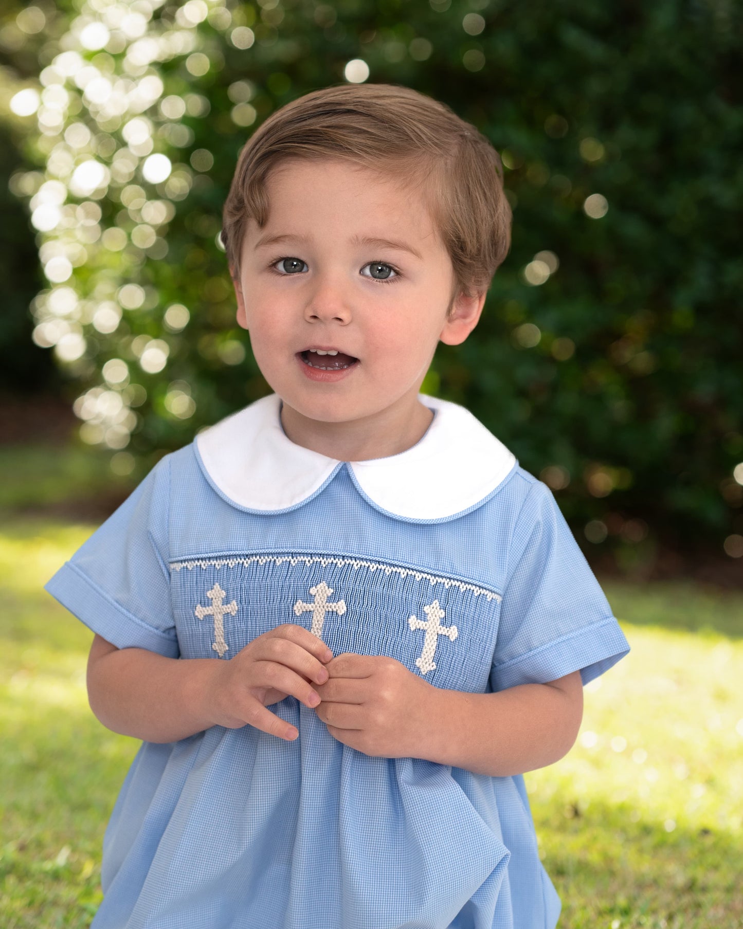 Child wearing a blue bubble with white collar and cross patterns outdoors.