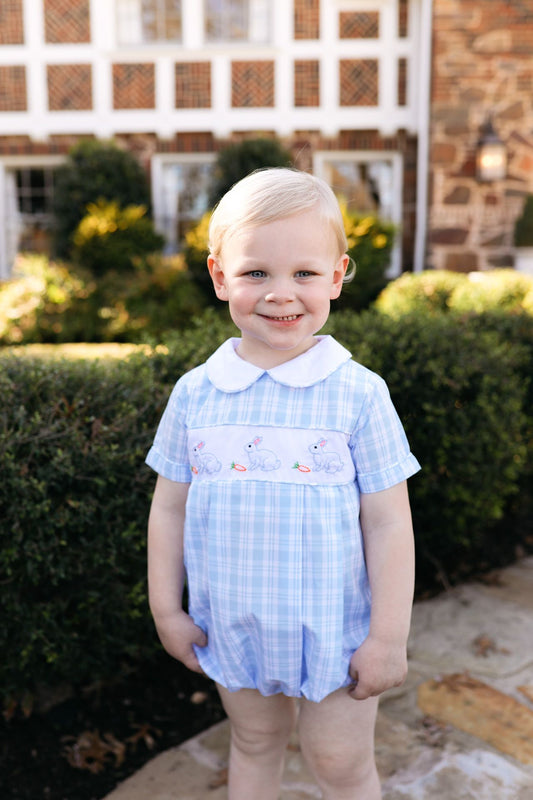Child wearing a blue checkered outfit with a white collar in an outdoor setting.