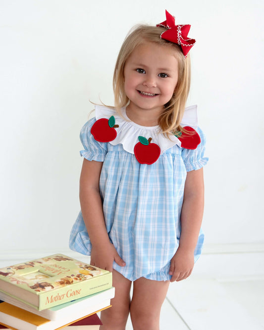 Child wearing a blue checkered outfit with red apple appliqués on a white background