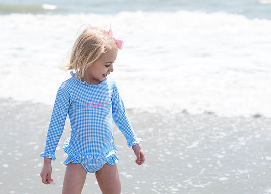 Child wearing a blue checkered swimsuit with long sleeves on a beach.