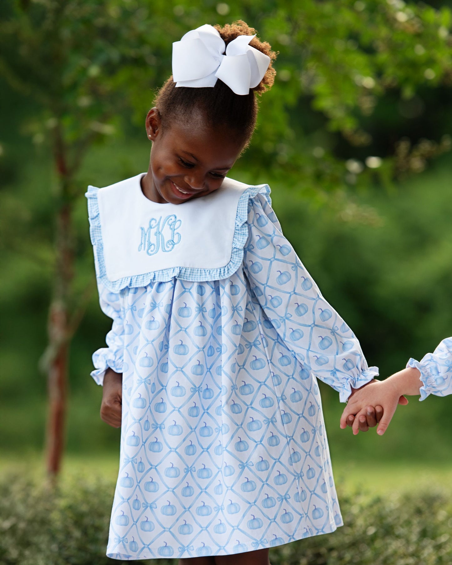 Child wearing a blue patterned dress with a white bow in an outdoor setting