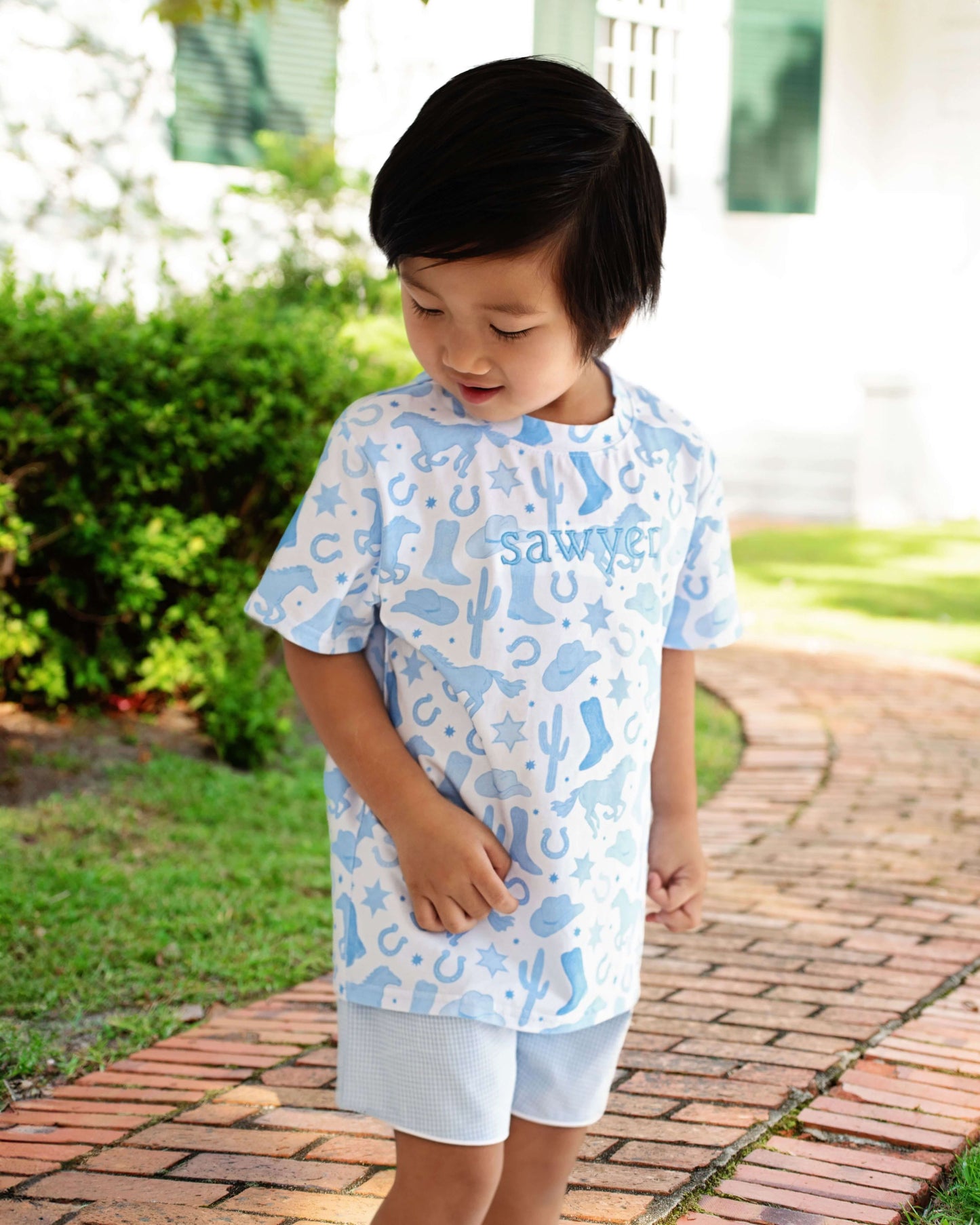 Child wearing a blue patterned outfit with 'Sawyer' printed on it, standing outdoors.