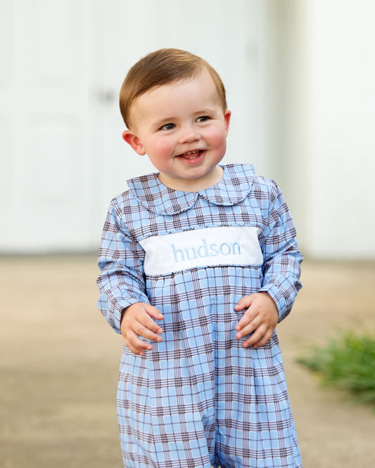 Child wearing a blue plaid outfit with 'Hudson' on a neutral background