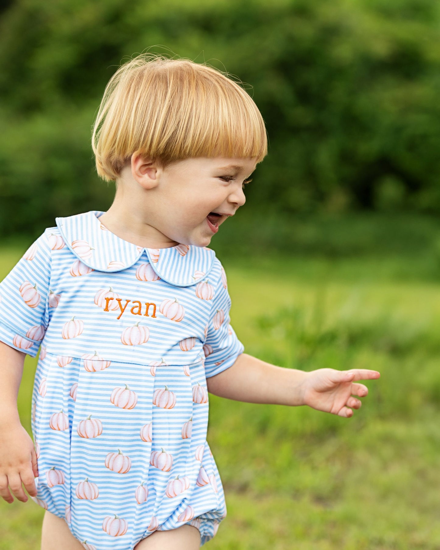 Child wearing a blue romper with pumpkin pattern outdoors