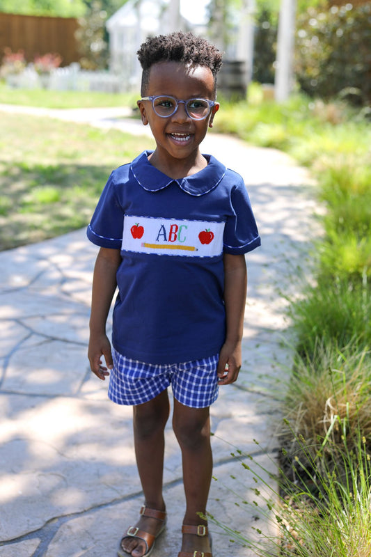 Child wearing a blue shirt with 'ABC' and apple graphics outdoors.