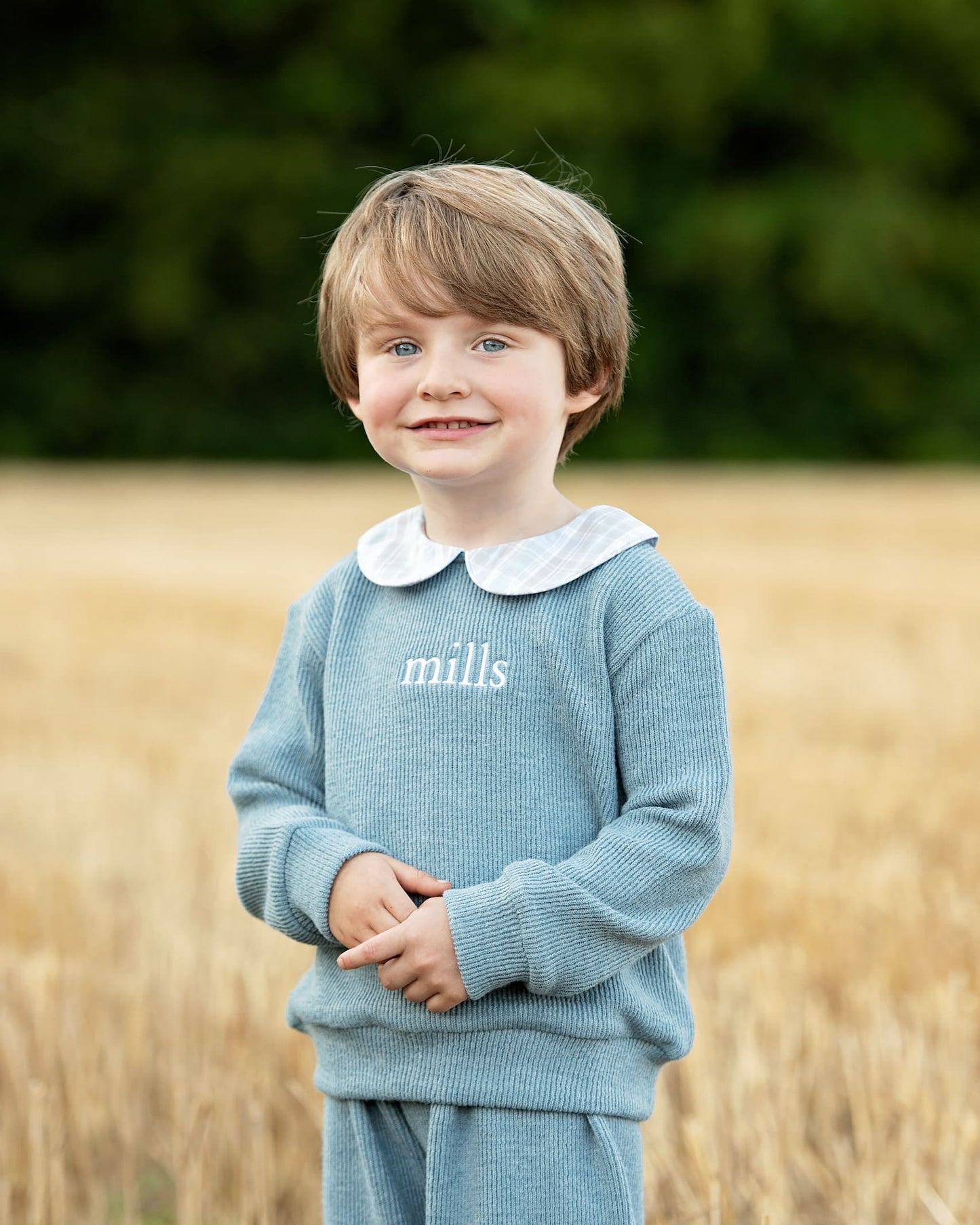 Child wearing a blue sweater with 'mills' branding in a field