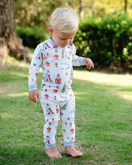Child wearing a colorful onesie with a pattern of presents and trees outdoors.