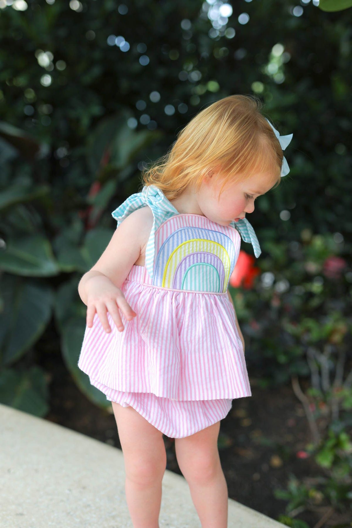 Child wearing a colorful rainbow-themed outfit with a pink skirt and ruffled top, standing outdoors.