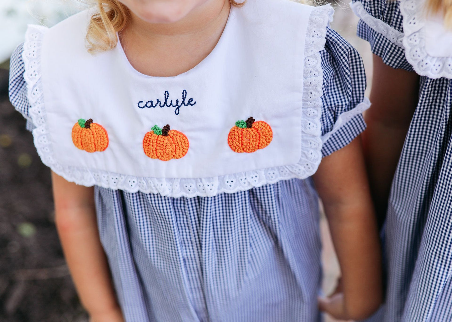 Child wearing a dress with embroidered pumpkins and name 'Carlyle'.