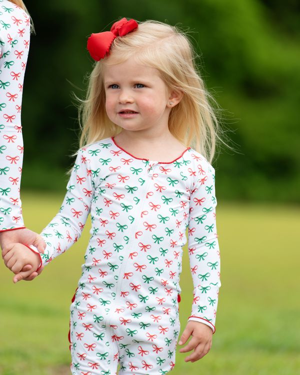 Child wearing a festive onesie with red and green bows outdoors